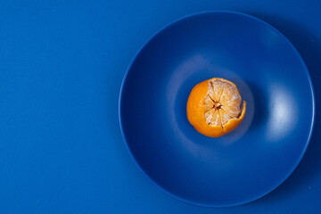 Half peeled tangerine on dark blue plate. Minimalist style photography. Color theory. Complementary...