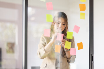 share idea, project successful, Business Asian business woman in meeting brainstorming and use post paper and writing note and stick on glass wall at workplace office.