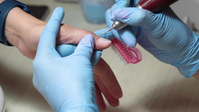 Process of manicure in a beauty salon close-up. Short nails care. Manicurist in blue gloves cuts cuticle with special nail file electric tool. 