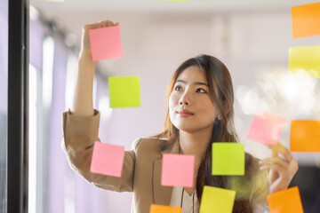 share idea, project successful, Business Asian business woman in meeting brainstorming and use post paper and writing note and stick on glass wall at workplace office.