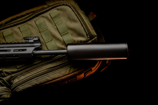 Black silencer for weapons. Suppressor that is at the end of an assault rifle. Weapon close-up. Dark back.