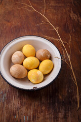 Yellow and brown Easter eggs in white bowl on wooden table. Spring holiday, happy easter concept. Vertical shot