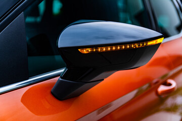 Close-up view of rear of the side mirror of modern orange and black car with orange led turn signal...