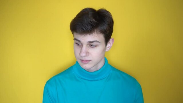 Young boy in blue shirt turns his head from side towards you and looking from under forehead with curious face, having suggestion. facial expression as I turn to you. Yellow horizontal background