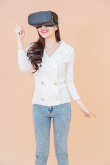 portrait of young asia woman wearing a white cardigan and VR glasses. She is amazed by what she is seeing. Virtual reality headset. isolated orange background