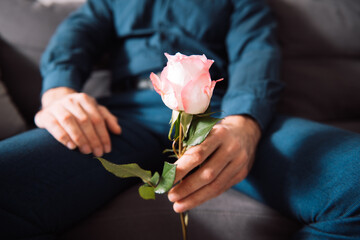 Guy holding red rose. Celebrating winter holiday or Valentine's Day, sitting in living room at home. Selective focus