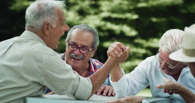 Portrait of Cheerful Senior Men Having fun and Challenging Each other in a Friendly Game of Arm Wrestling. Elderly Friends Laughing Together and Cheering in Green Park. They Embody Good Sportsmanship 
