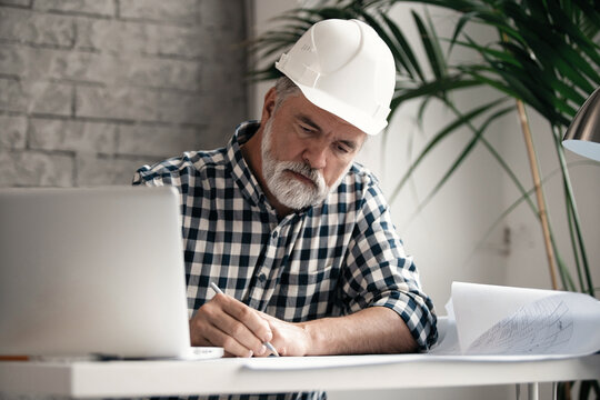 Mature confident smiling architect in casual wear working with blueprint papers and drawings in modern lightful office.