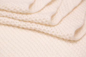 Fototapeta na wymiar Knitted surface of woolen things as a background. Close-up of soft white texture of knitted patterns. Warm winter clothes. Background textile surface with copy space for text.