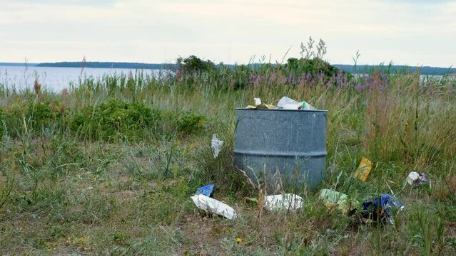 Overfilled garbage can on a beach during sunny summer day. Trash bin in nature. 