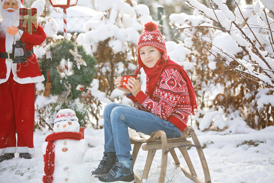 Sweet school child, boy, playing in garden with snow, making snowman, happy kid winter time