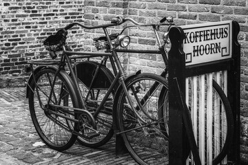 Black and white picture of a traditional old Dutch bicycles parked in a bicycle standing near the wall of the coffee house.