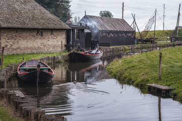 Small canal with its traditional fishing boats, fish smoker in the background. - 564677401