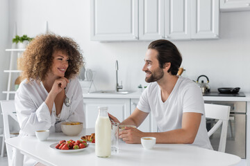 cheerful young woman having breakfast with bearded boyfriend in kitchen.
