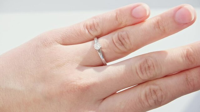 Close up of woman hand with the ring on the girl's finger. Elegant diamond ring on white background. Diamond engagement brilliant ring. High quality FHD footage with slow motion