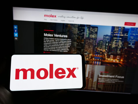 Stuttgart, Germany - 01-22-2023: Person holding cellphone with logo of US connector manufacturing company Molex LLC on screen in front of business web page. Focus on phone display.