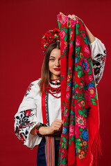 Portrait of ukrainian woman in traditional ethnic clothing and floral red wreath with handkerchief on viva magenta studio background. Ukrainian national embroidered dress call vyshyvanka