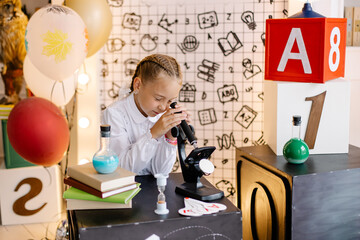 Schoolgirl in the lesson with a microscope. Smart child is learning. Back to school theme. Lesson in elementary school. diligent student. Scientific knowledge. Science and children