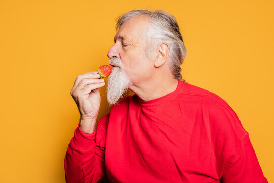 Content senior man biting sweet strawberry