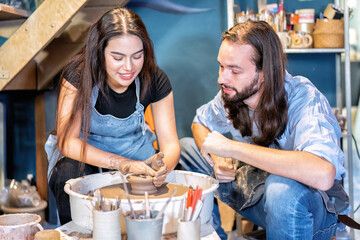 Man potter teaching pot making women learn on potters wheel making clay objects in pottery workshop