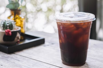 Side view of iced dark cold brew americano coffee on the plastic cup  on the wooden bar table with bokeh background in coffee shop.