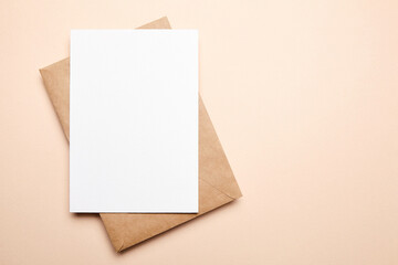 Greeting card mockup with envelop on beige background, top view, flat lay. Blank holiday card or flyer