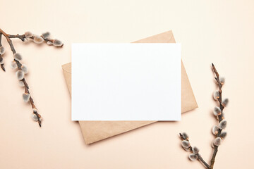 Greeting card mockup with branch of pussy willow and envelop on beige background, top view, flat...