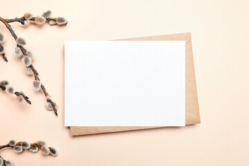 Greeting card mockup with branch of pussy willow and envelop on beige background, top view, flat lay. Blank Easter Holiday card with catkins