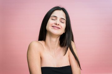 Obraz premium Smiling woman with closed eyes on pink background