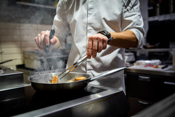 man chef cooking fried salmon fish in frying pan on kitchen