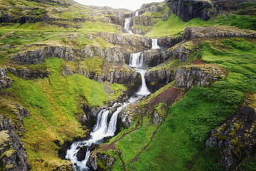Klifbrekkufossar seven tier waterfall flowing hidden in the Mjoifjordur Fjord on summer at Iceland © Mumemories