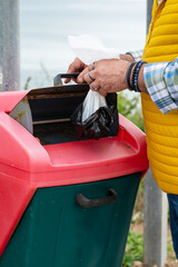 Older man introducing a bag full of dog excrement in a specific container for it, concept of cleanliness, conscience, responsibility.