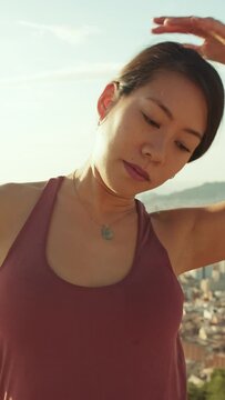 VERTICAL VIDEO: Young woman stretches her neck muscles while standing on an observation deck