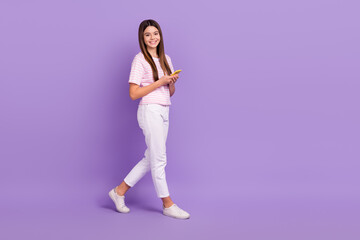 Fototapeta na wymiar Full length profile photo of cheerful girl walking hold telephone empty space isolated on violet color background