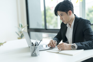 Young businessman opening a notebook View emails from customers sent. and write down the details.