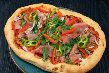 Italian Pizza on plate with jamon slices, pepper and fresh arugula leaves on top