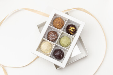 Healthy handmade chocolate candies in white box on white background. Six cheese truffles and...