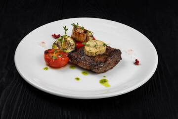 Grilled black angus strip loin steak with vegetables on white plate on black wooden background