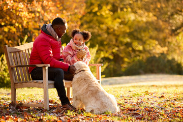 Father And Daughter With Hot Drink Sitting On Bench With Pet Dog On Walk In Autumn Countryside