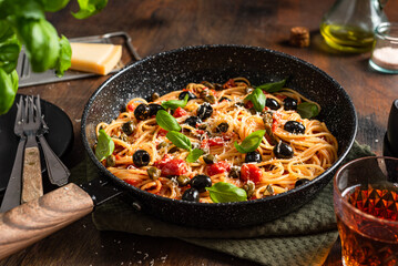 Spaghetti pasta with tomatoes sauce, black olives, capers, parmesan and fresh basil. Dark wooden...