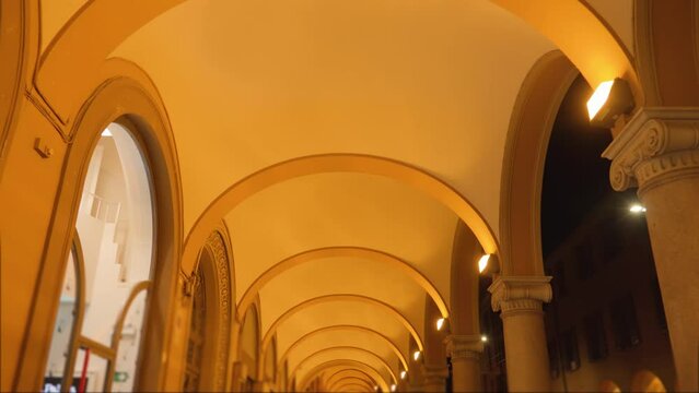 High old building medieval portico ceiling with arches and lamps fastening on marble columns illuminated with soft yellow light in evening in Bologna