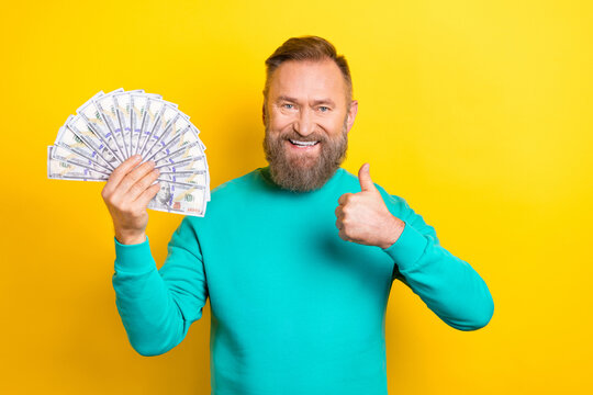 Photo portrait of nice retired man thumb up hold money fan rich wear trendy aquamarine look isolated on yellow color background
