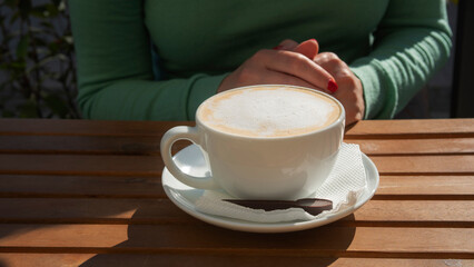 Girl at the table in a cafe with a cup of cappuccino. Delicious drink with appetizing milk foam.