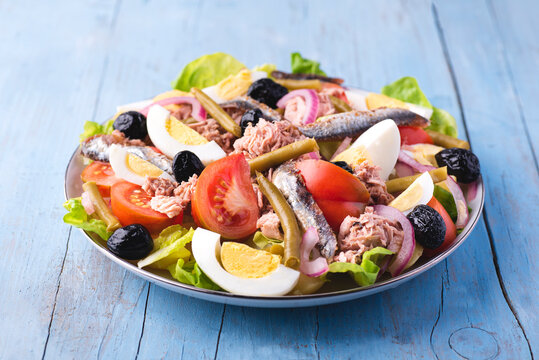 Salad nicoise recipe or  'Nicoise salad', Nizza Salat with tuna, salted anchovies, potatoes, boiled green beans, vegetables, on a rustic blue background. Summer French salads, healthy food