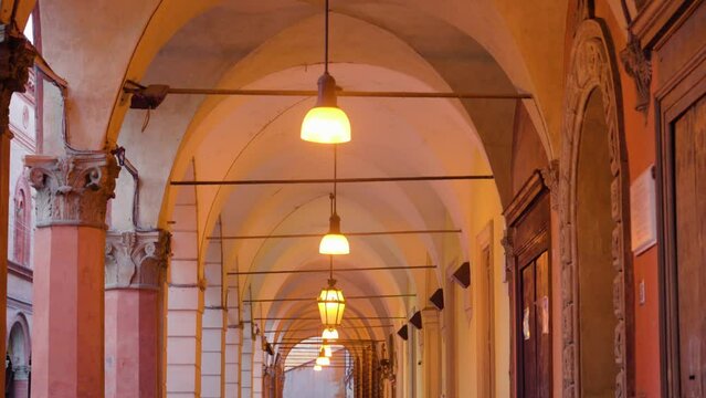 Lamps illuminate historical building medieval portico with bright yellow light hanging along long gallery with semi-circular arches in Bologna