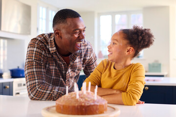 Father And Daughter At Home In Kitchen Celebrating Blowing Out Candles On Homemade Birthday Cake