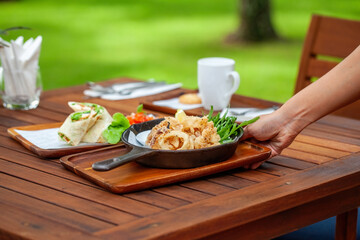 Man hand puts a tray and pan of food with fresh frying calamari on wooden table