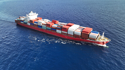 Fototapeta premium Aerial drone top down photo of huge container ship full of colourful containers cruising deep blue open ocean sea