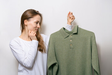 A young attractive woman is looking skeptical at a green woolen sweater and choosing an outfit....