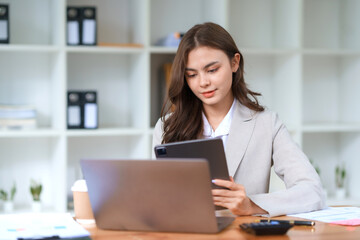 Smiling and attractive asian businesswoman enjoying working using laptop computer at office.